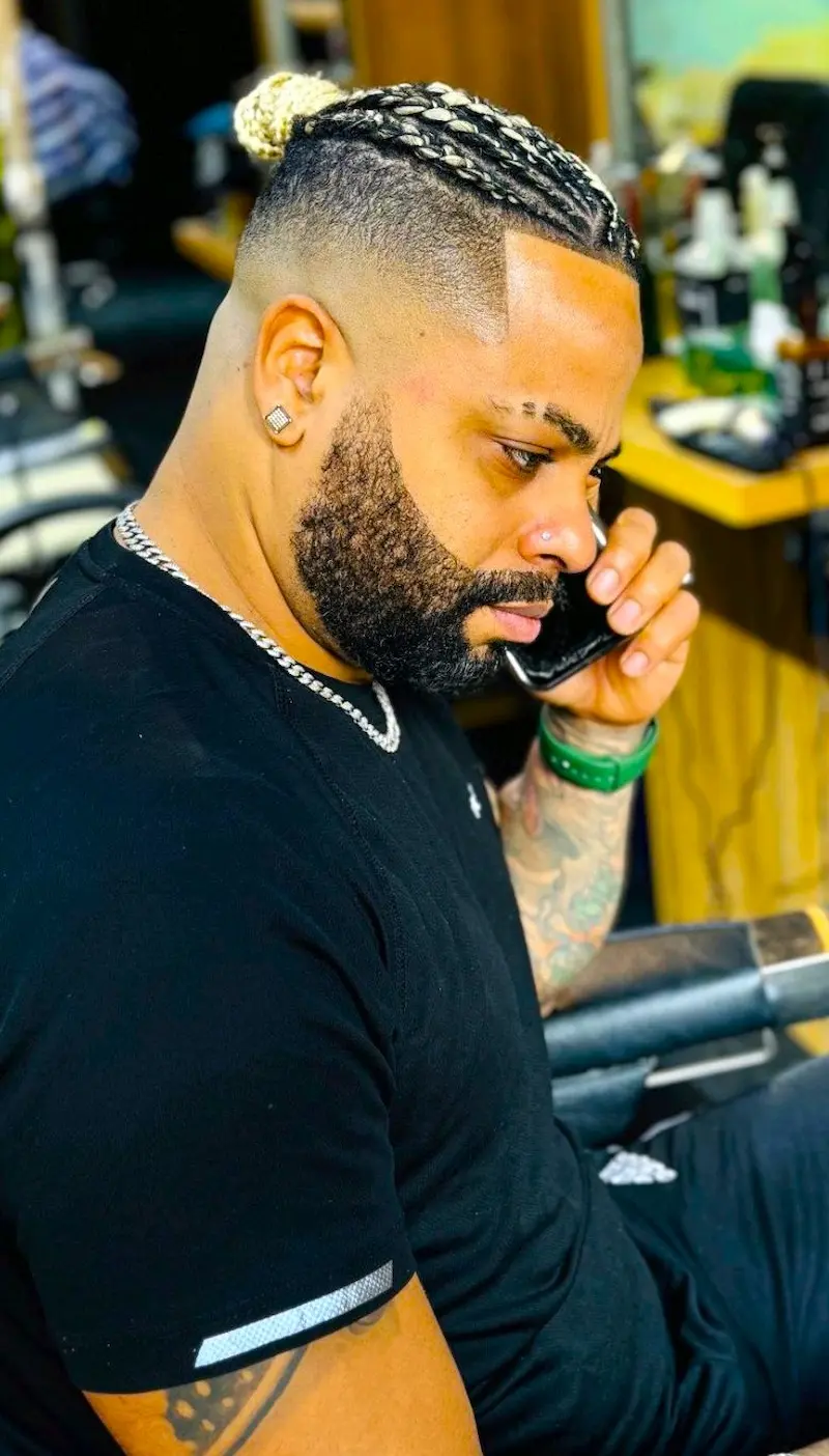 man with braided hair and beard sitting in barber chair talking on phone in Kings Afro Barbershop JVC Dubai