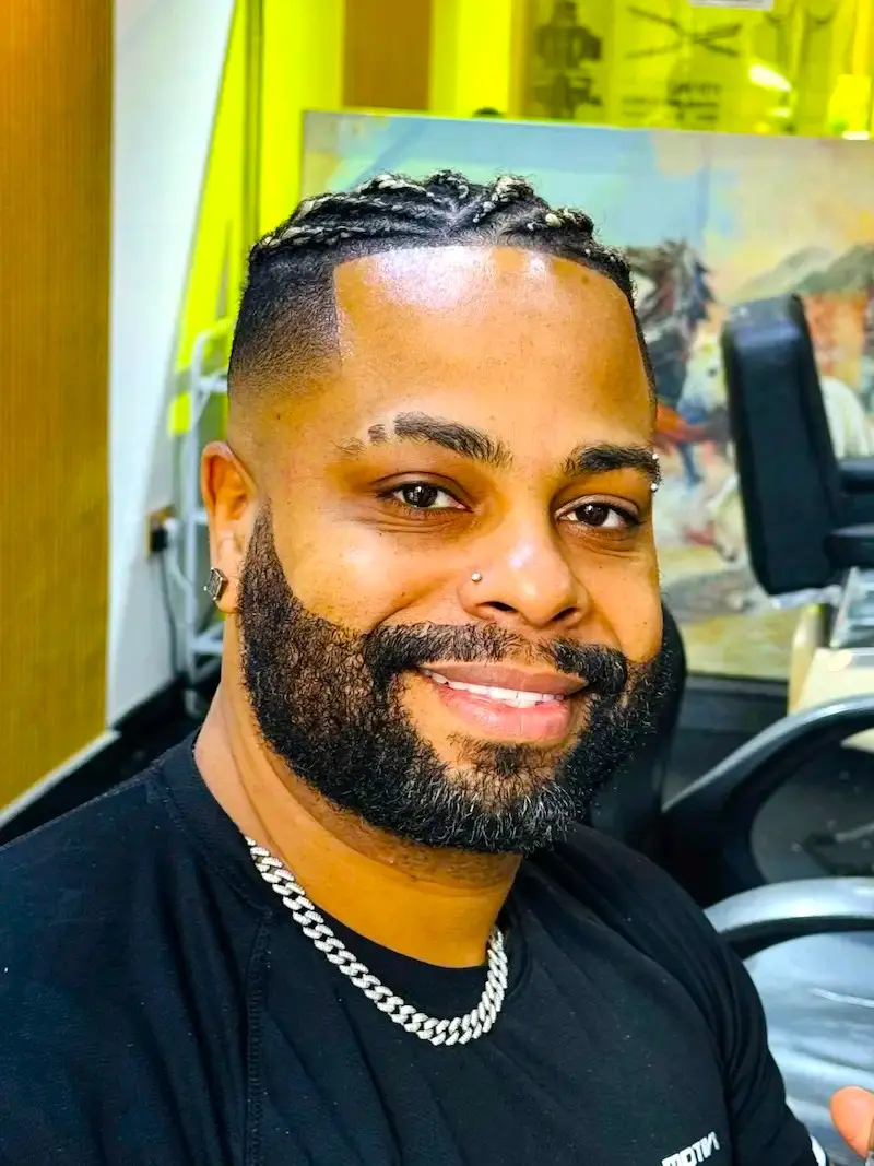 smiling man with braided hair and groomed beard after haircut sitting in barber chair professional result