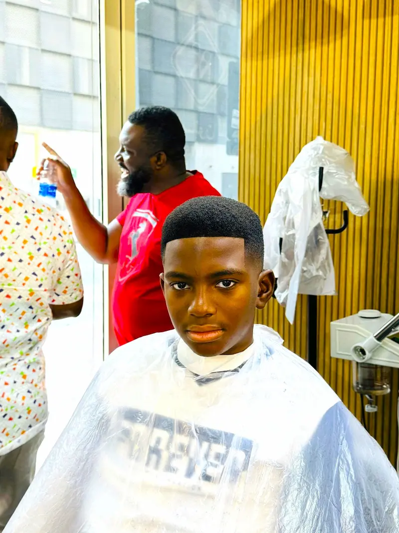 young boy after a fresh haircut sitting in a barber chair with a clean low fade and sharp lineup inside a modern barbershop
