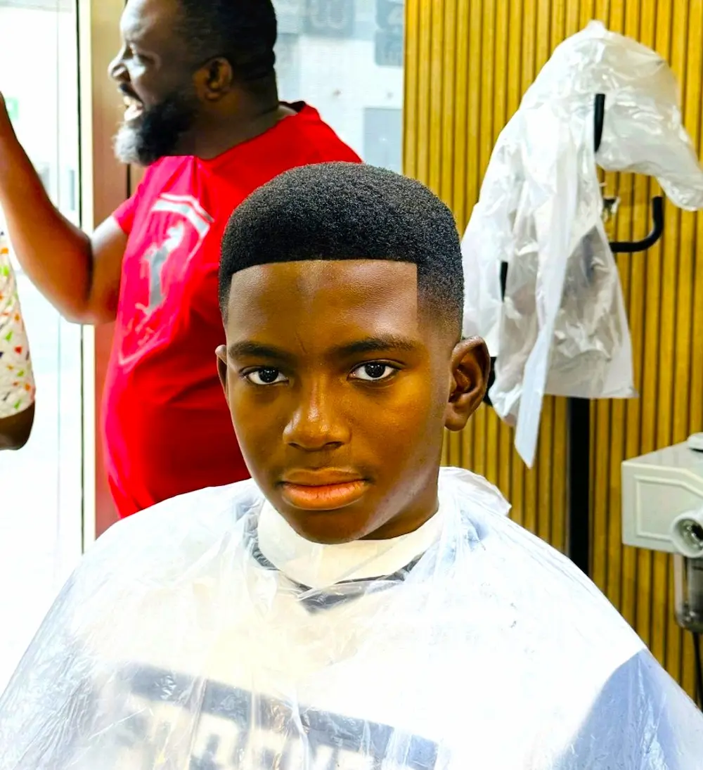 young boy after a fresh haircut sitting in a barber chair with a clean low fade and sharp lineup inside a modern barbershop