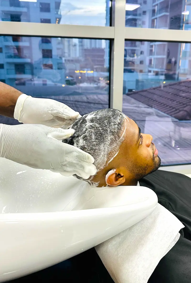 man getting his hair washed at a barbershop sink, barber wearing gloves applying shampoo and massaging scalp